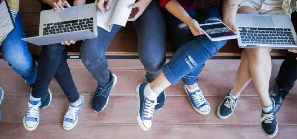 Jugendliche sitzen nebeneinander und haben Laptops in der Hand.